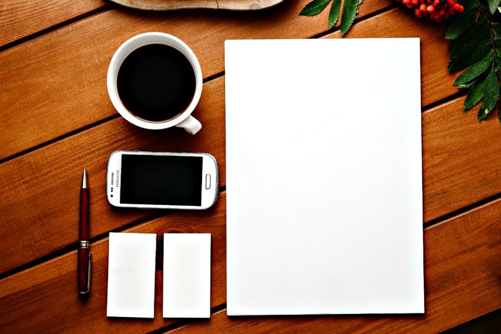 Eine Tasse Kaffee, ein Smartphone, Stift und Papier bilden die Basis für jeden angehenden Texter.